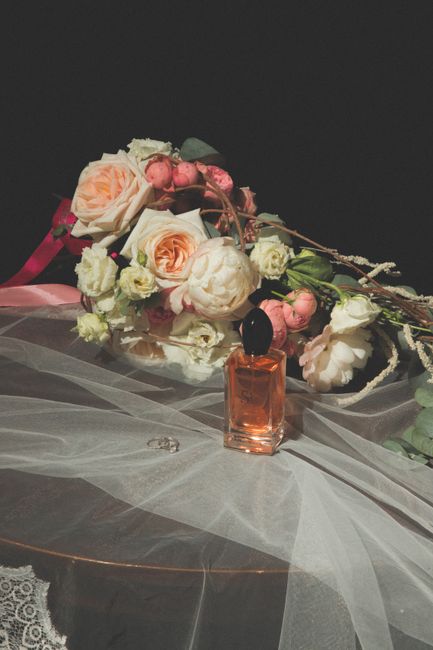 A delicate floral arrangement featuring soft pink and white roses, complemented by smaller white blossoms and green foliage, arranged on a transparent tulle fabric draped over a dark surface. A small
